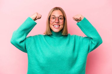 Pembe arka planda izole edilmiş genç beyaz kadın güçlü bir hareket gösteriyor. Kollarıyla, kadınsı gücün sembolü.