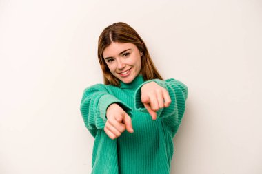 Beyaz arka planda izole edilmiş genç beyaz kadın parmaklarıyla ön tarafı işaret ediyor..