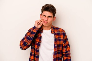 Beyaz arka planda izole edilmiş beyaz tenli genç bir adam parmakları dudaklarında bir sır saklıyor..