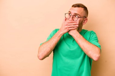 Beyazlı genç bir adam bej arka planda izole edilmiş. Düşünceli bir şekilde bir fotokopi odasına bakıyor. Ağzını eliyle kapatıyor..