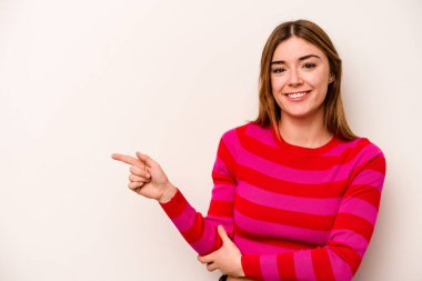 Beyaz arka planda izole edilmiş genç beyaz kadın işaret parmağıyla işaret ederek gülümsüyor..