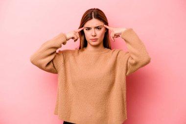 Pembe arka planda izole edilmiş genç beyaz kadın bir göreve odaklanmış, parmaklarını işaret ediyor..