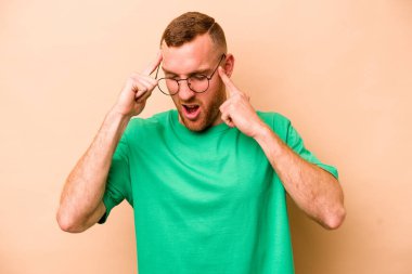 Beyaz tenli genç adam bej arka planda izole edilmiş tapınaklara dokunuyor ve baş ağrısı çekiyor..