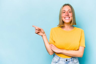 Mavi arka planda izole edilmiş genç beyaz kadın işaret parmağıyla işaret ederek gülümsüyor..