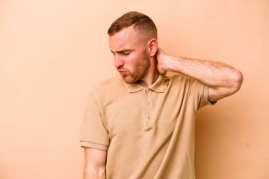 Beyazlı genç bir adam bej arka planda izole edilmiş. Stres yüzünden boynu ağrıyor. Masaj yapıyor ve elle dokunuyor..