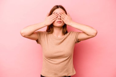 Pembe arka planda izole edilmiş genç beyaz kadın elleriyle gözlerini kapatmaktan korkuyor..