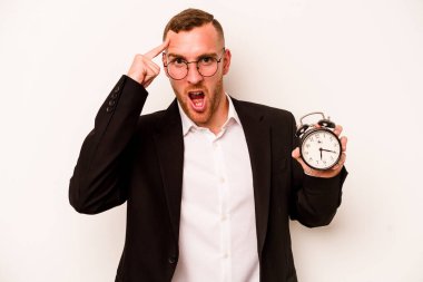 Beyaz arka planda alarm saati tutan genç beyaz bir adam işaret parmağıyla yaptığı hayal kırıklığını gösteriyor..