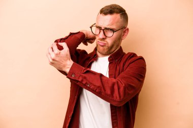 Beyazlı genç bir adam bej arka planda izole edilmiş. Stres yüzünden boynu ağrıyor. Masaj yapıyor ve elle dokunuyor..