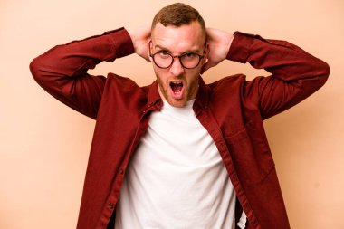Beyaz tenli genç adam bej arka planda izole edilmiş bağırıyor, çok heyecanlı, tutkulu, bir şeyden memnun..