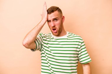 Beyaz tenli genç adam bej arka planda izole edilmiş bir şekilde bir şey unutuyor. Alnına avuç içi ve kapalı gözlerle vuruyor..