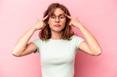 Pembe arka planda izole edilmiş genç beyaz kadın bir göreve odaklanmış, parmaklarını işaret ediyor..