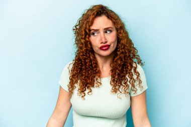 Genç, beyaz, mavi arka planda izole bir kadın omuzlarını silker ve gözleri açık kalır..
