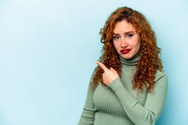 Mavi arka planda izole edilmiş genç, beyaz bir kadın gülümsüyor ve boş alanda bir şeyler gösteriyor..