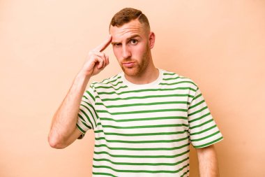 Beyazların arka planında izole edilmiş genç beyaz bir adam şakağı parmağıyla işaret ediyor, düşünüyor ve bir göreve odaklanıyor..