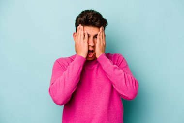 Mavi arka planda izole edilmiş genç beyaz adam yüzünün yarısını palmiye ile kaplayarak eğleniyor..