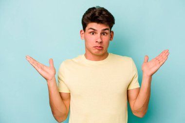 Kafkasyalı genç adam mavi arka planda izole edilmiş. Kafası karışmış ve omuz silkiyor. Kopya alanını tutmak için..
