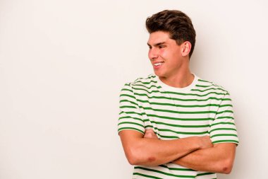 Beyaz arka planda izole edilmiş genç beyaz adam kollarını kavuşturarak gülümsüyor..