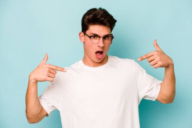 Kafkasyalı genç adam mavi arka planda izole edildi. Parmakları aşağıda, olumlu bir his var..