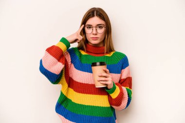 Beyaz arka planda izole edilmiş kahve taşıyan beyaz tenli genç bir kadın şakağı parmağıyla işaret ediyor, düşünüyor ve bir göreve odaklanıyor..