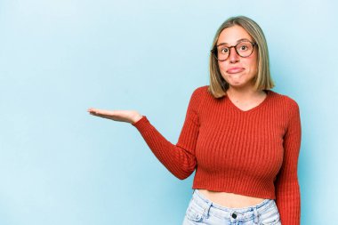 Mavi arka planda izole edilmiş genç beyaz kadın bir avuç içinde fotokopi alanı ve belinde bir el daha gösteriyor..