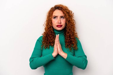 Beyaz arka planda izole edilmiş beyaz tenli genç bir kadın el ele tutuşup, ağzının kenarında dua ediyor, kendinden emin..