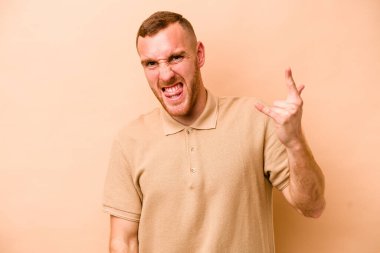 Beyaz tenli genç adam bej arka planda izole edilmiş. Parmaklarıyla kaya hareketi gösteriyor.