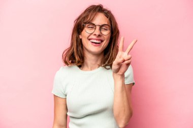 Pembe arka planda izole edilmiş genç beyaz kadın iki numarayı parmaklarıyla gösteriyor..