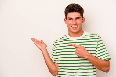 Beyaz arka planda izole edilmiş genç beyaz bir adam, palmiye üzerinde bir fotokopi alanı tutarken heyecanlı..