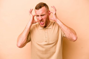 Beyazlı genç bir adam bej arka planda izole edilmiş kulakları elleriyle kapatıyor..