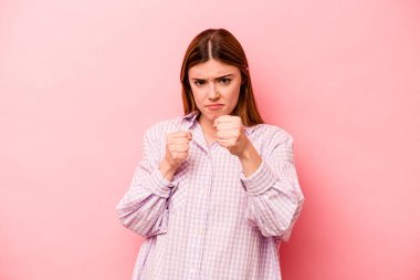 Pembe arka planda izole edilmiş genç beyaz kadın yumruğunu kameraya gösteriyor, agresif yüz ifadesi..