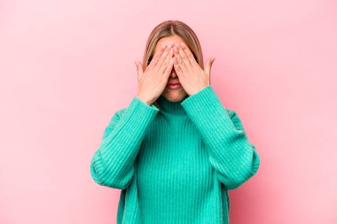 Pembe arka planda izole edilmiş genç beyaz kadın elleriyle gözlerini kapatmaktan korkuyor..