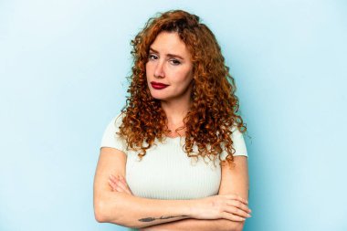 Genç, beyaz, mavi arka planda izole edilmiş, iğneleyici bir ifadeyle kameraya bakan mutsuz bir kadın..