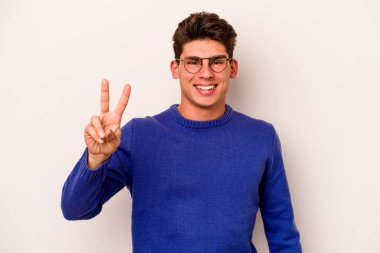 Beyaz arka planda izole edilmiş genç beyaz bir adam neşeli ve kaygısız parmakları olan bir barış sembolü gösteriyor..