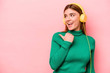 Pembe arka planda müzik dinleyen beyaz bir kadın. Baş parmak uzakta, gülüyor ve kaygısız..