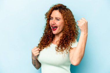 Genç beyaz kadın mavi arka planda izole edilmiş tasasız ve heyecanlı bir şekilde tezahürat yapıyor. Zafer konsepti.