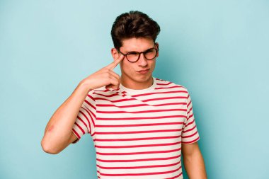 Mavi arka planda izole edilmiş genç beyaz bir adam şakağı parmağıyla işaret ediyor, düşünüyor ve bir göreve odaklanıyor..