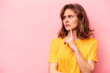 Pembe arka planda soyutlanmış beyaz bir kadın şüpheli ve şüpheci bir ifadeyle yana bakıyor..