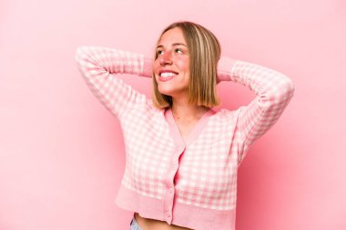 Pembe arka planda soyutlanmış genç beyaz bir kadın kendini güvende hissediyor, elleri başının arkasında..