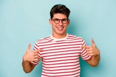 Kafkasyalı genç adam mavi arka planda izole edildi. Parmakları aşağıda, olumlu bir his var..