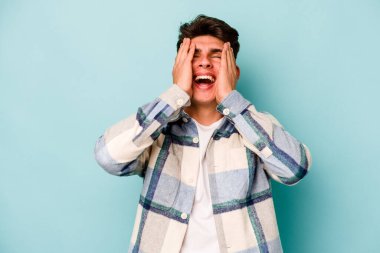 Mavi arka planda izole edilmiş genç beyaz adam ellerini başının üstünde tutarak neşe içinde gülüyor. Mutluluk kavramı.