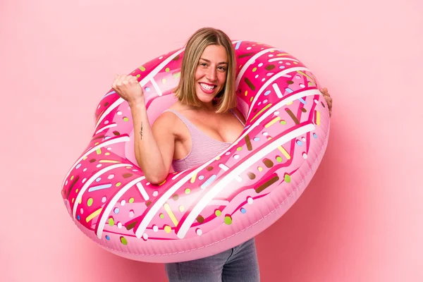 Pembe arka planda şişme yatak tutan beyaz bir kadın.