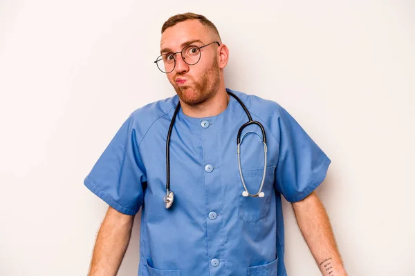 Young caucasian nurse man isolated on white background shrugs shoulders and open eyes confused.