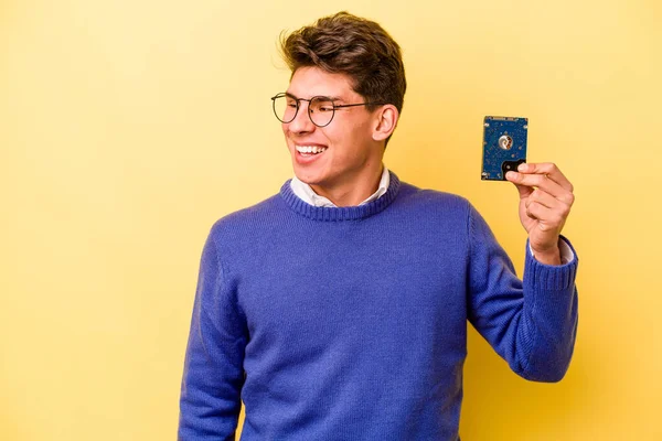 Young caucasian informatics man isolated on yellow background looks aside smiling, cheerful and pleasant.