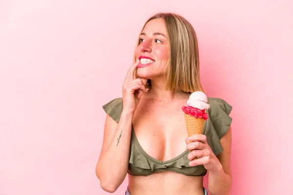 若い白人女性がビキニを着てピンクの背景に隔離されたアイスクリームを持っているコピースペースを見て何かについてリラックスした考え — ストック写真