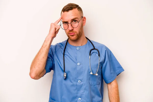 Young caucasian nurse man isolated on white background pointing temple with finger, thinking, focused on a task.