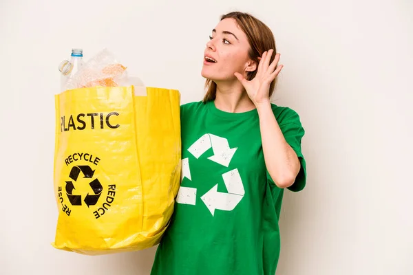 白い背景に隔離されたリサイクルのためのペットボトルでいっぱいの袋を持っている若い女性はゴシップを聞こうとしている — ストック写真