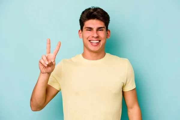 青い背景に孤立した若い白人男性喜びと屈託のない指で平和のシンボルを示す — ストック写真