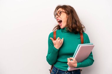Young student caucasian woman isolated on white background points with thumb finger away, laughing and carefree.
