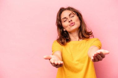 Beyaz bir kadın pembe arka planda izole edilmiş dudaklar kıvrılmış ve hava öpücüğü göndermek için avuç içleri tutulmuş..