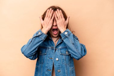 Beyaz tenli, bej arka planda izole edilmiş genç bir kadın yüzünün yarısını palmiye ile örterek eğleniyor..